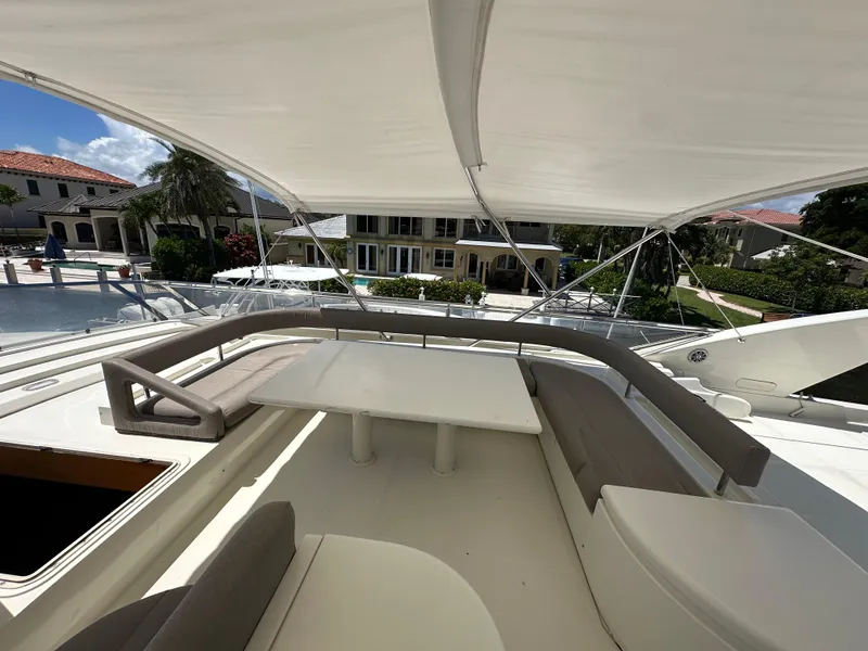 Slide: The Image of 1998 Ferretti Yachts 80 flybridge with seating area and table, docked near luxury homes. - 14