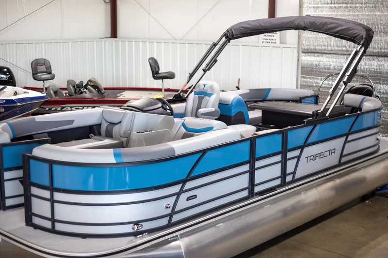 Slide: The Image of 2025 Trifecta 24E CS3 pontoon boat with blue and gray accents in a showroom. - 3