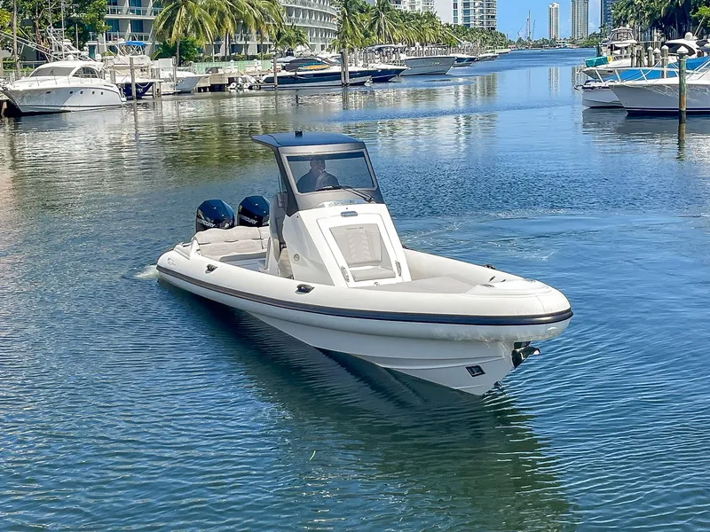 Slide: The Image of 2025 Ribco Venom 30 boat cruising on a scenic waterway with palm trees and yachts. - 2