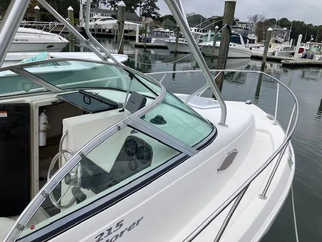 Slide: The Image of 2004 Aquasport 215 Explorer boat docked in a marina, showcasing cockpit and cabin area. - 7