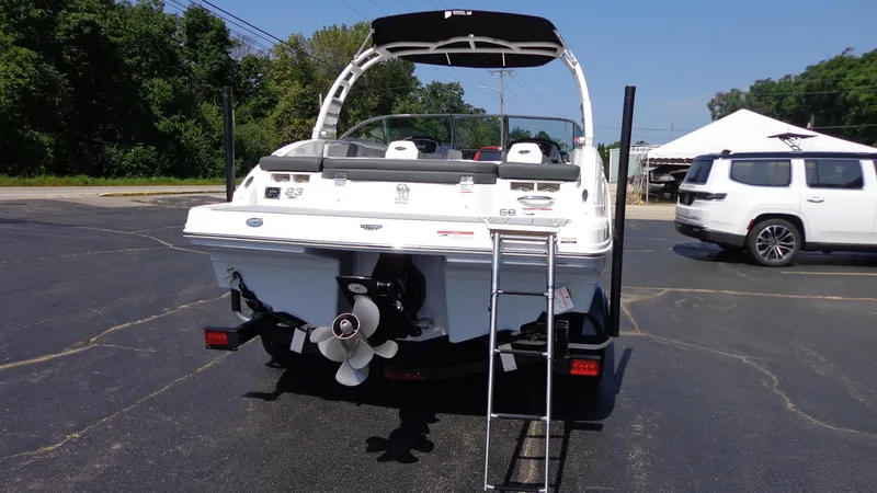 Slide: The Image of 2025 Chaparral 23 SSi boat, rear view with ladder and propeller, parked outdoors. - 2
