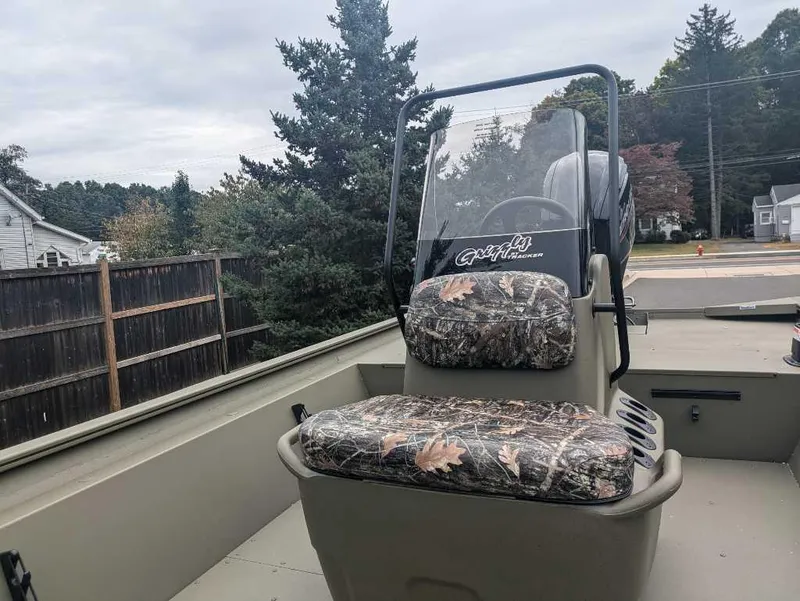 Slide: The Image of 2025 Tracker Grizzly 1860 CC boat with camo seats, parked outdoors. - 2