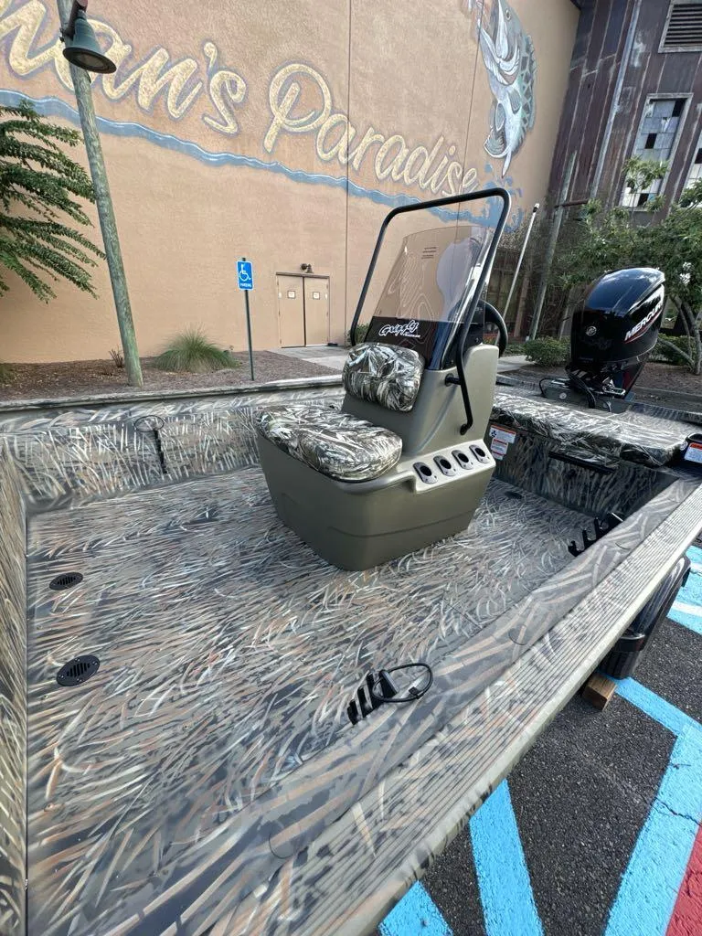 Slide: The Image of 2025 Tracker Grizzly 1860 CC boat with camo seats and console, parked outdoors. - 5