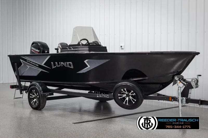 Slide: The Image of 2025 Lund Adventure SS boat on trailer in showroom, featuring sleek black design. - 2