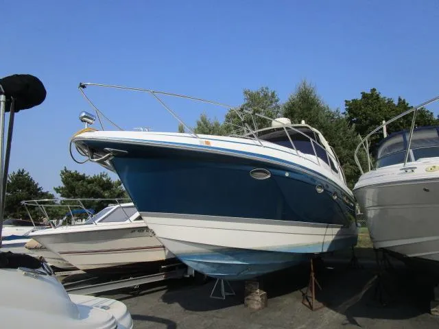 The Image of 2006 Formula 34 PC boat on dry dock, blue and white hull, surrounded by trees. - 1