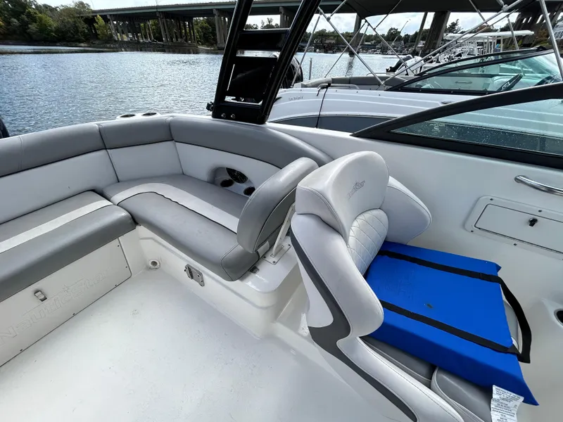 Slide: The Image of 2021 NauticStar 243 DC boat interior with gray seating and blue cushion, docked by the water. - 17