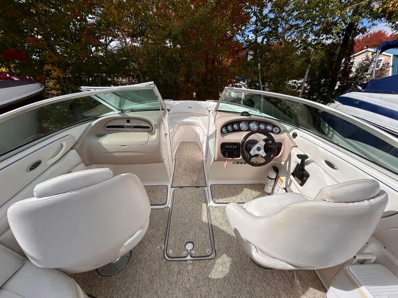 Slide: The Image of 2002 Chaparral 220 SSi boat interior with white seating and dashboard, surrounded by autumn foliage. - 30