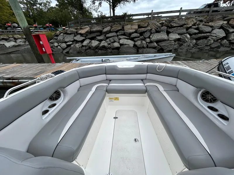 Slide: The Image of 2021 NauticStar 243 DC boat interior with gray seating, docked by rocky shore. - 10
