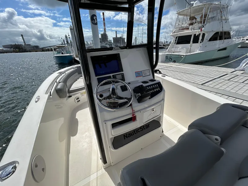 Slide: The Image of 2021 NauticStar 2602 Legacy boat console with steering wheel and controls, docked at marina. - 13
