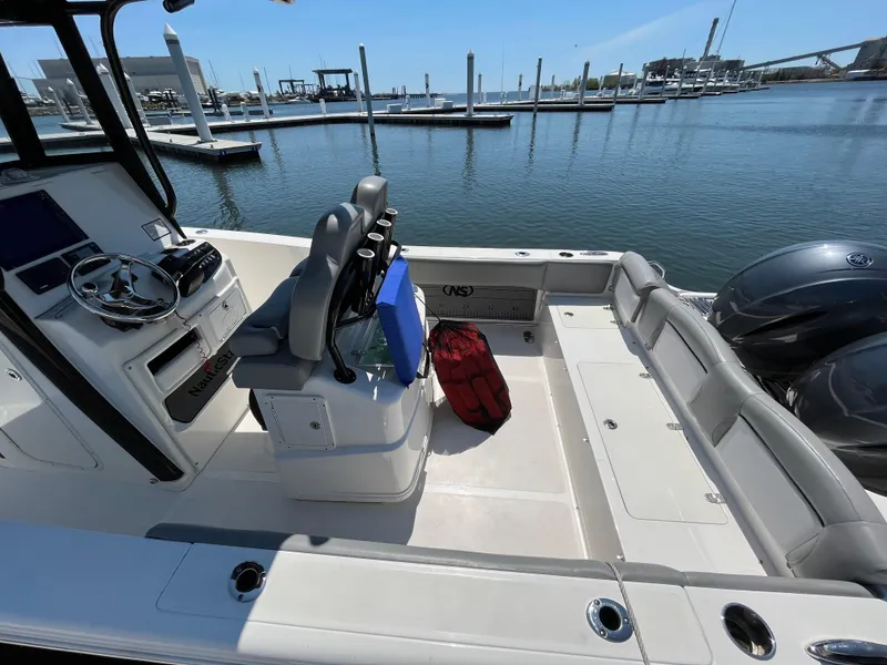 Slide: The Image of 2021 NauticStar 2602 Legacy boat interior at marina, featuring seating and dual engines. - 22