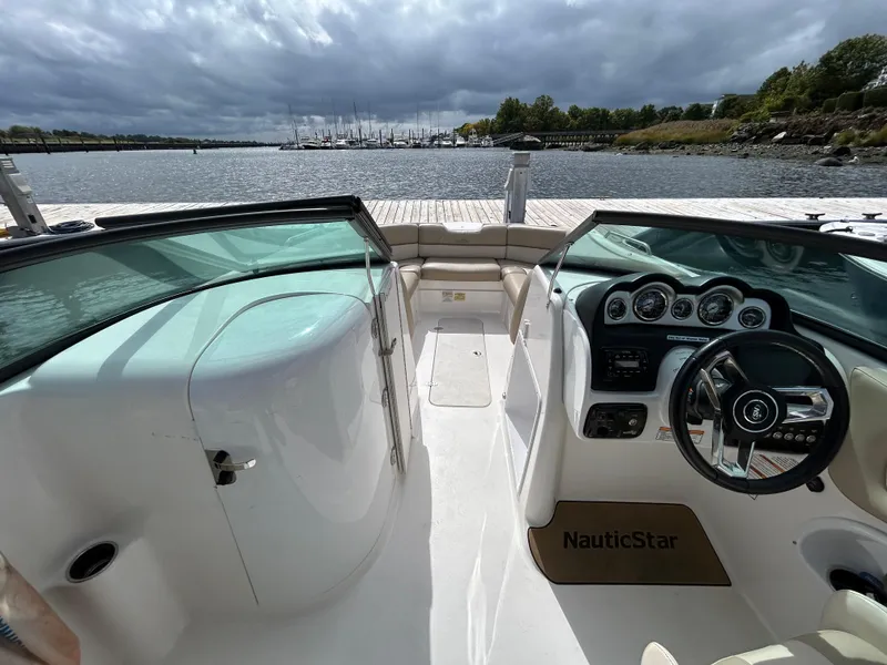 Slide: The Image of 2022 NauticStar 243 DC boat interior with steering wheel and dashboard, overlooking a scenic waterfront. - 16