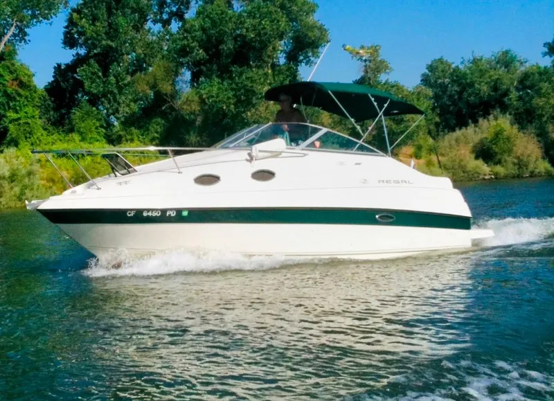 Slide: The Image of 1997 Regal Commodore 242 boat cruising on a river with lush green trees. - 0