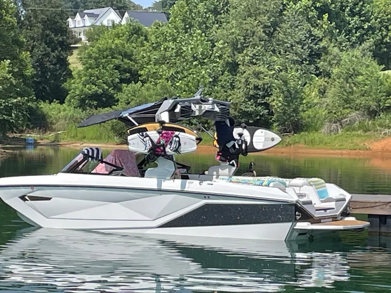 Slide: The Image of 2023 Nautique Super Air G23 boat docked on a serene lake with lush greenery. - 96