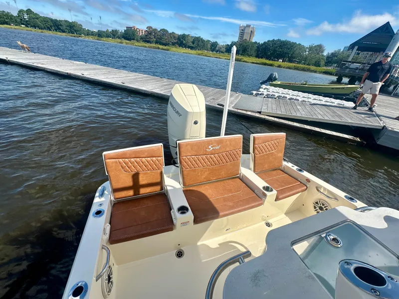 Slide: The Image of 2026 Scout 261 XSS boat with brown seating, docked by a scenic waterfront. - 6