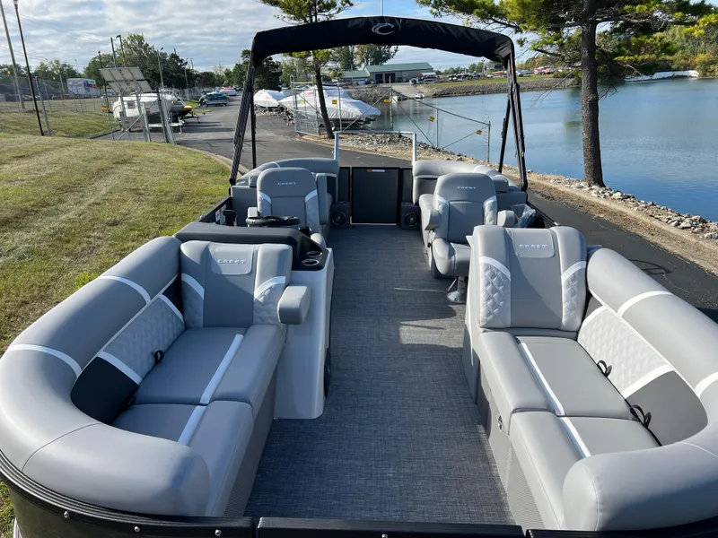 Slide: The Image of 2025 Crest CLASSIC 220 SLC pontoon boat with spacious seating, docked by a serene lake. - 12
