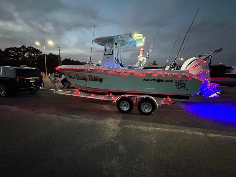 Slide: The Image of NauticStar 242OSL 2025 boat on trailer, decorated with festive lights at dusk. - 11