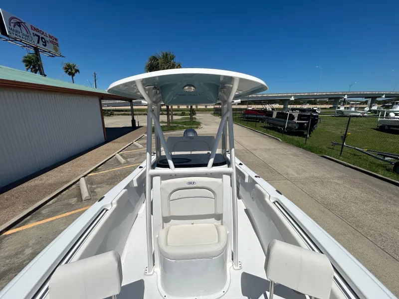 Slide: The Image of 2025 Sea Hunt Ultra 229 boat with T-top, docked under clear blue sky. - 17