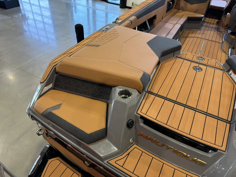 Slide: The Image of 2025 Nautique Super Air Nautique GS24 interior with tan and gray seating, wood-style flooring. - 12