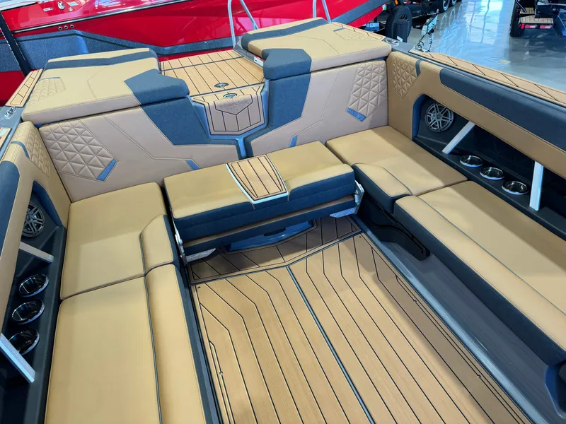 Slide: The Image of 2025 Nautique Super Air Nautique GS24 interior with tan and blue seating, cup holders, and speakers. - 16