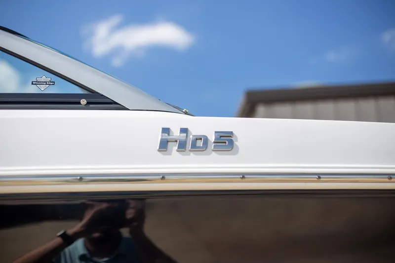 Slide: The Image of 2025 Four Winns HD5 boat exterior with logo under blue sky. - 4