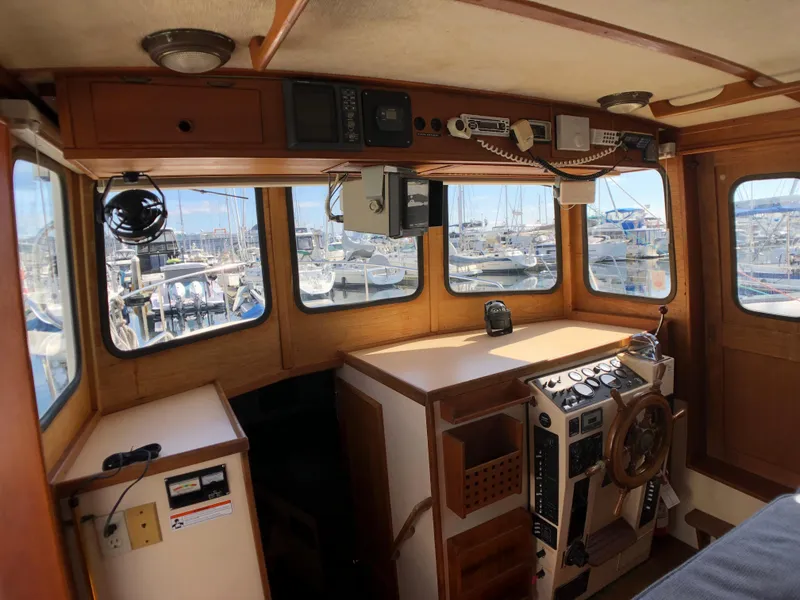 Slide: The Image of 1989 Nordic Tug 32 interior with wooden helm, navigation equipment, and marina view. - 10