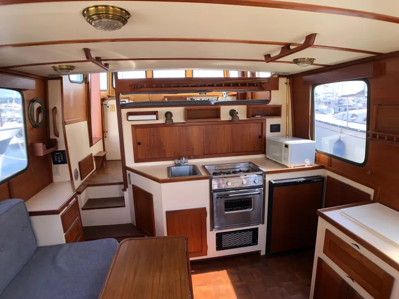 Slide: The Image of 1989 Nordic Tug 32 interior with kitchen, stove, sink, and microwave, showcasing wooden cabinetry. - 14