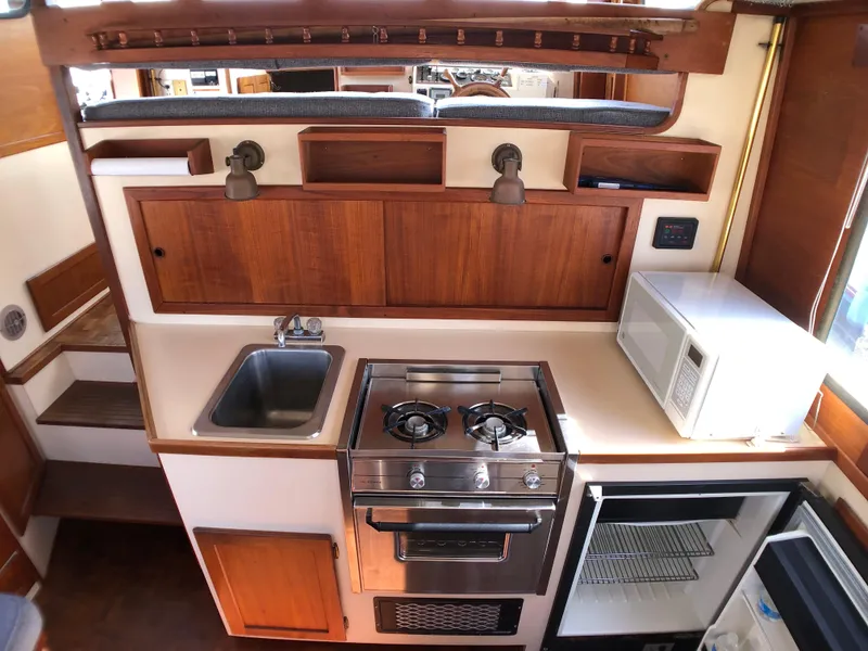 Slide: The Image of 1989 Nordic Tug 32 kitchen with stove, sink, microwave, and wooden cabinetry. - 18