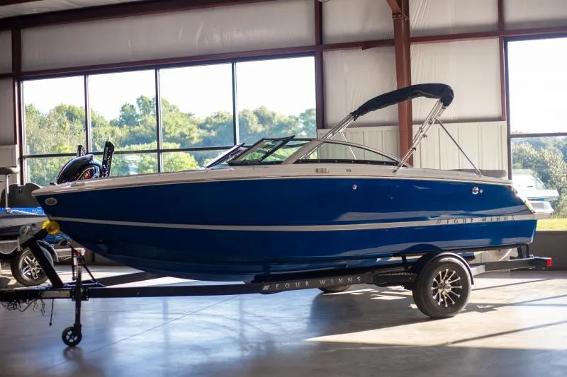 The Image of 2025 Four Winns H1 boat in a showroom, blue exterior, on a trailer. - 1