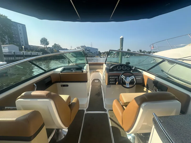 Slide: The Image of 2014 Sea Ray 270 SLX boat interior with tan seats and steering wheel, docked by the water. - 6
