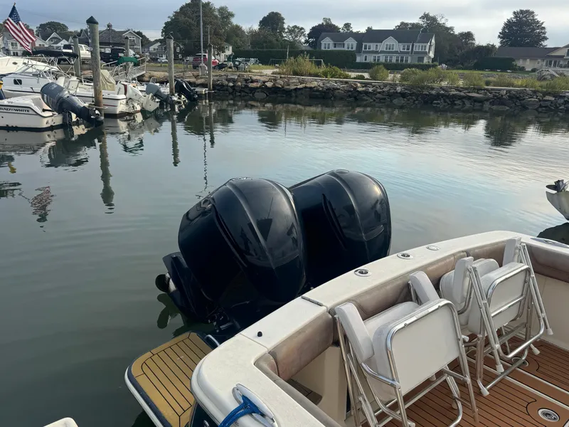 Slide: The Image of 2015 Scout 320 LXF boat docked with dual outboard engines, calm water, and nearby houses. - 15