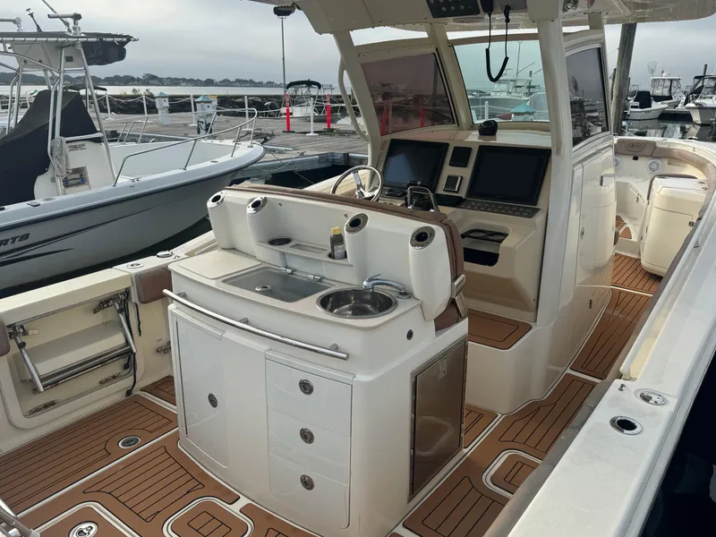 Slide: The Image of 2015 Scout 320 LXF boat interior with helm, sink, and storage on teak deck. - 8