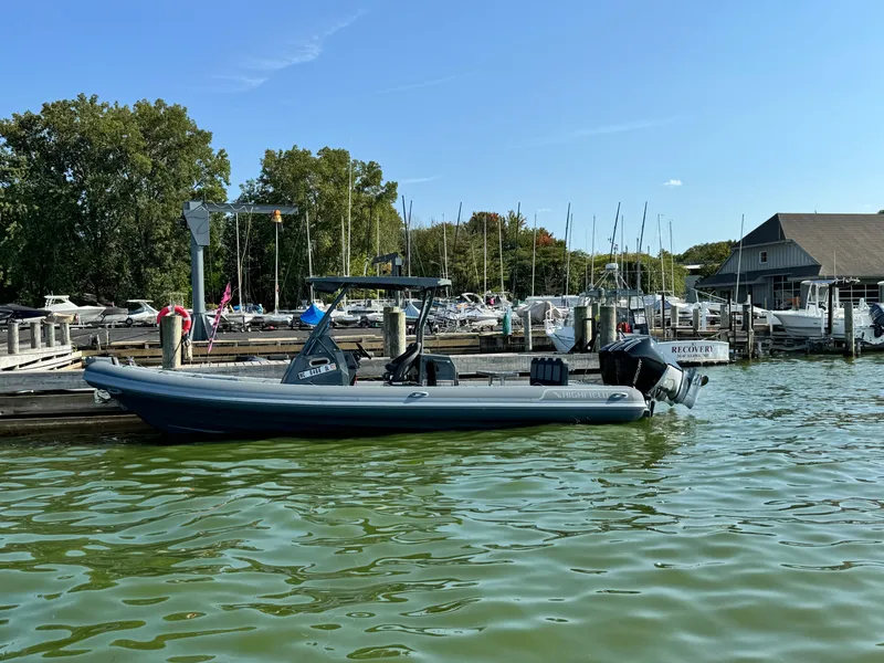 Slide: The Image of 2024 Highfield Sport 900 boat docked at a marina with trees and sailboats in the background. - 0