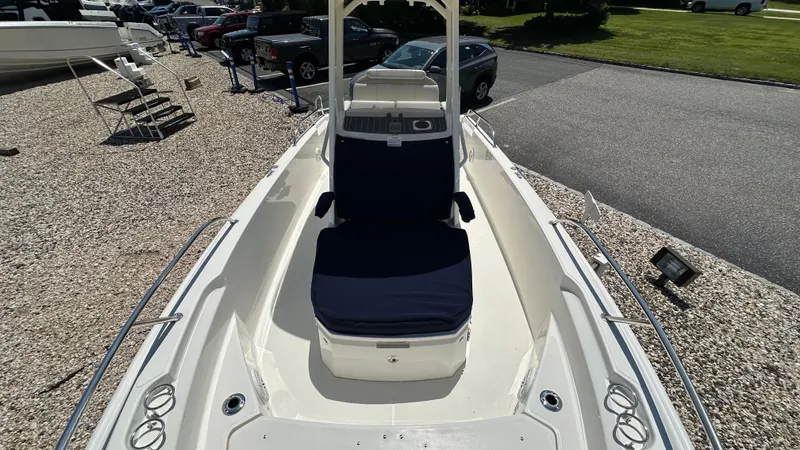 Slide: The Image of 2025 Boston Whaler 220 Dauntless boat, white exterior, blue seating, parked on gravel. - 16