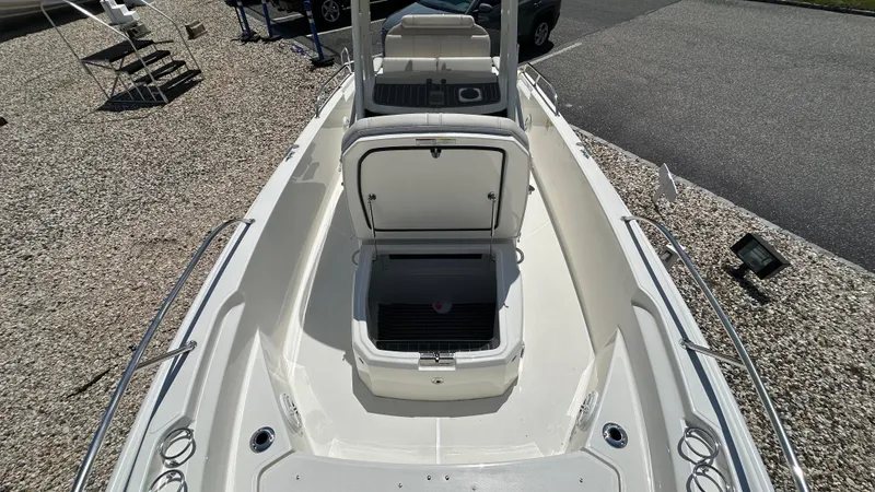 Slide: The Image of 2025 Boston Whaler 220 Dauntless boat with open storage compartments, docked on gravel. - 18