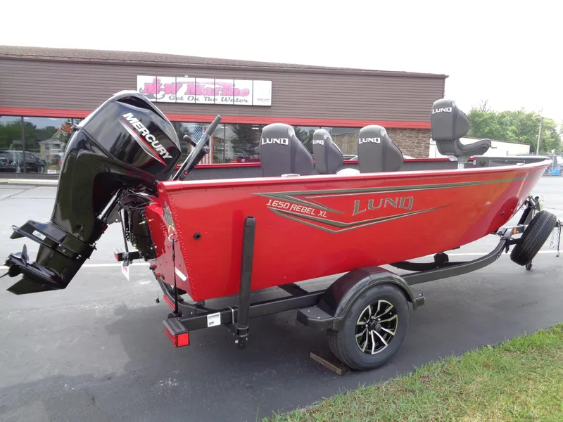 Slide: The Image of 2025 Lund 1650 Rebel XL Tiller boat, red exterior, on trailer with Mercury outboard motor. - 2
