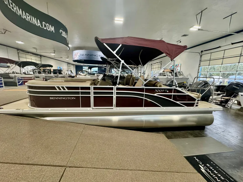 Slide: The Image of 2024 Bennington 22 SXSB pontoon boat displayed indoors with maroon canopy. - 1
