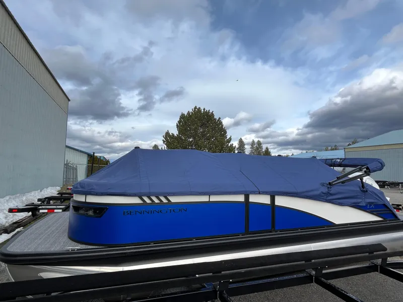 Slide: The Image of 2024 Bennington 24LXSFB boat with blue cover, parked outdoors under cloudy sky. - 7