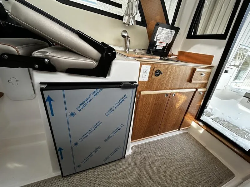 Slide: The Image of 2023 Cutwater C-248 C interior with kitchenette, featuring wood cabinets and compact fridge. - 18