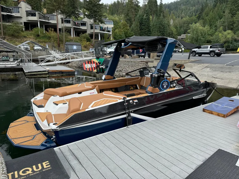Slide: The Image of 2025 Nautique G23 boat docked at a marina, surrounded by lush greenery. - 2