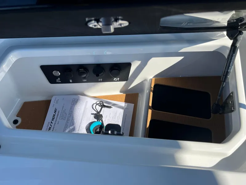 Slide: The Image of 2025 Nautique G23 storage compartment with controls and documents. - 36