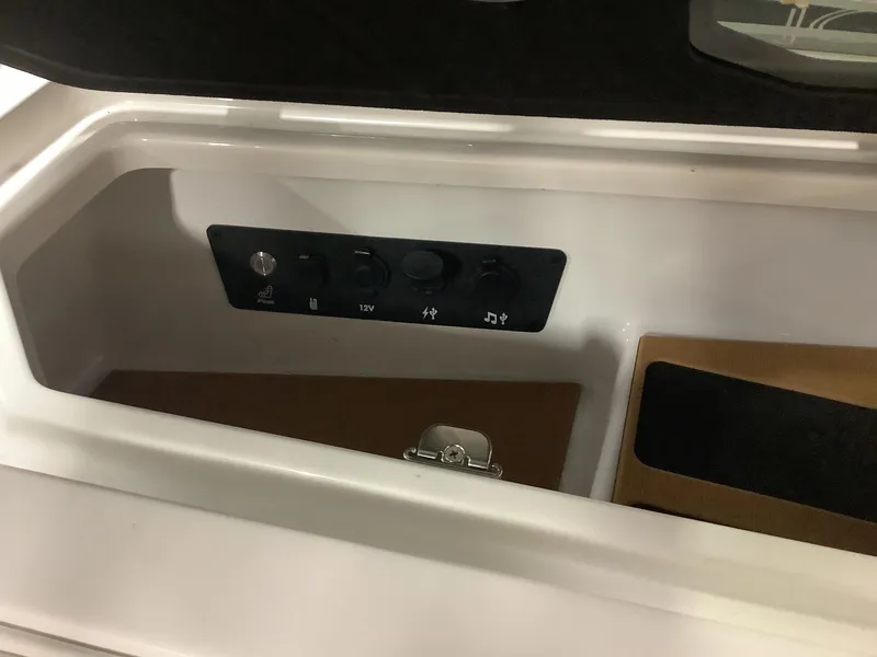 Slide: The Image of 2025 Nautique G25 storage compartment with control panel and 12V power outlet. - 16