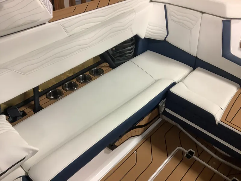 Slide: The Image of 2025 Nautique G25 boat interior with white and navy seating, cup holders, and teak flooring. - 19