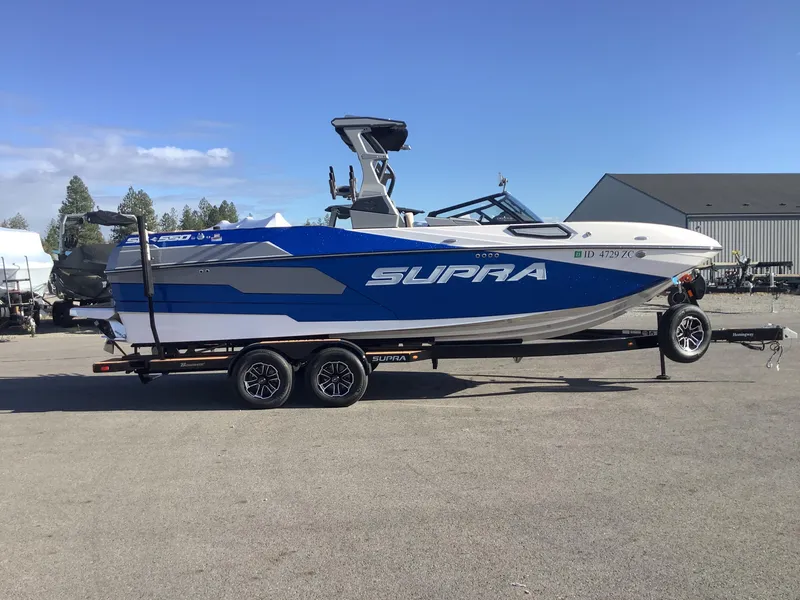 Slide: The Image of 2023 Supra SE 550 boat on trailer, blue and white design, parked outdoors. - 6