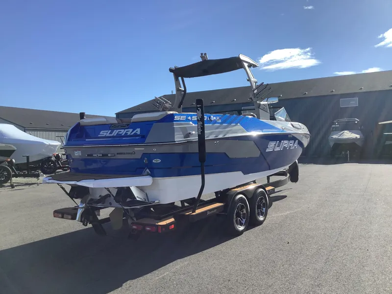 Slide: The Image of 2023 Supra SE 550 boat on trailer, blue and white design, parked outdoors. - 7