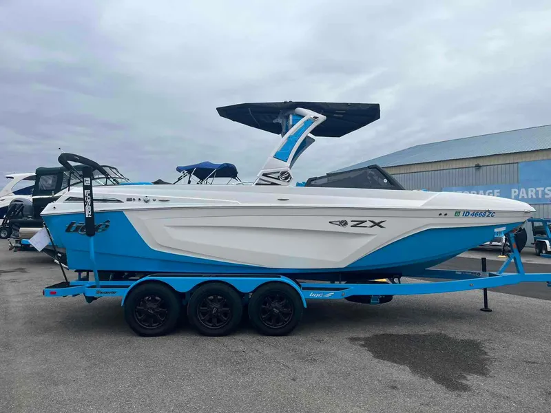 Slide: The Image of 2023 Tigé 25ZX boat on trailer, blue and white design, parked outdoors. - 4