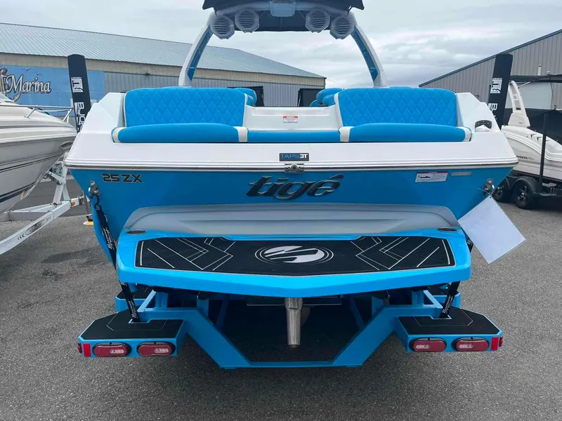 Slide: The Image of 2023 Tigé 25ZX boat, blue and white, rear view at marina. - 5