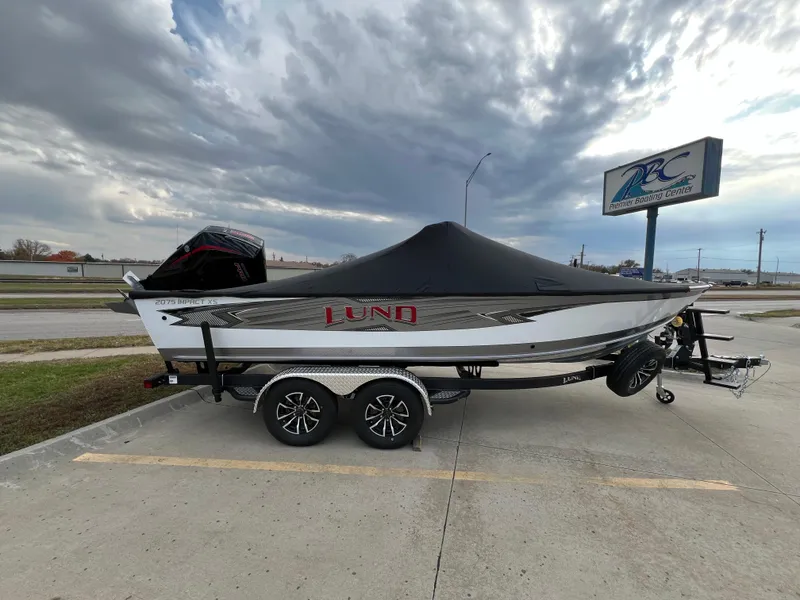 Slide: The Image of 2025 Lund 2075 IMPACT XS boat with cover on trailer, parked outdoors. - 0