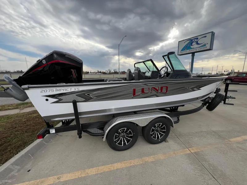 Slide: The Image of 2025 Lund 2075 IMPACT XS boat on trailer, parked outdoors under cloudy sky. - 12