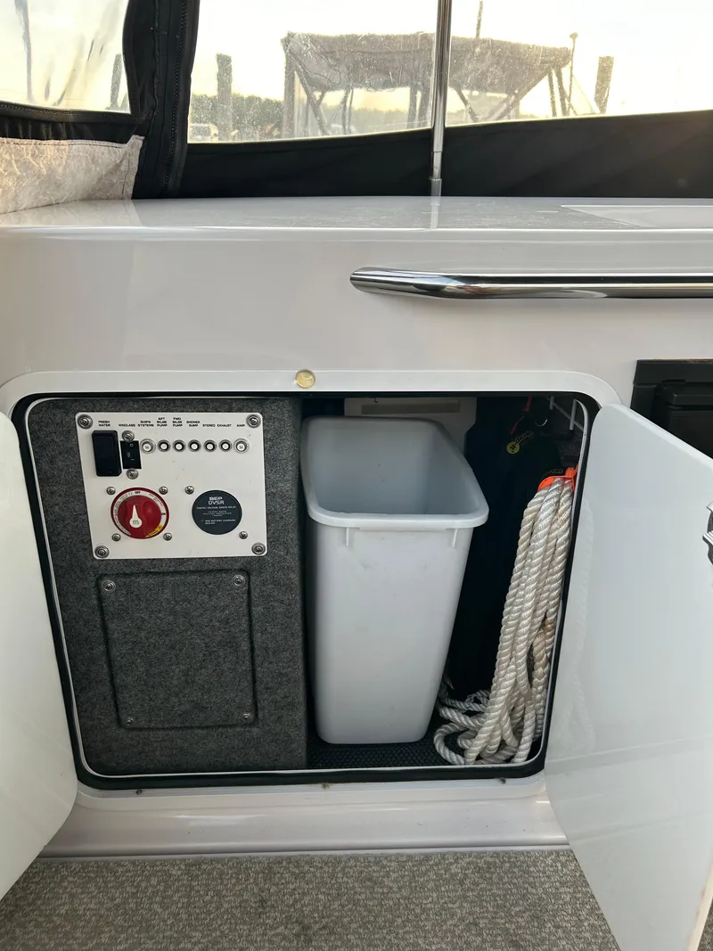 Slide: The Image of 2014 Four Winns Vista 275 boat storage compartment with control panel, trash bin, and rope. - 19