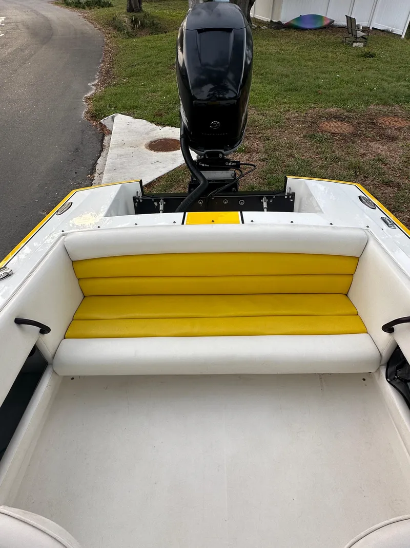 Slide: The Image of 1990 Superboat 21 with yellow and white seating, outboard motor, parked near grass. - 11
